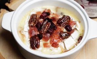 bol de brie fondant recouvert de cannebergers séchées et de pacanes à l'érable sur une planche de bois. Un pot de confit d'oignon CANNE BERGE à côté du bol.