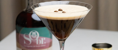 Verre de martini rempli d'un espresso martini sans alcool. Une bouteille d'amaretto érable et amande sans alcool par SObr.
