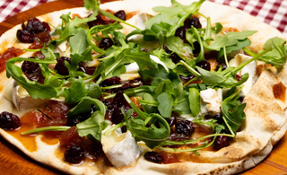 Pizza brie, roquette et canneberge déposée sur une planche de bois