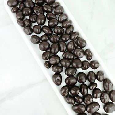Canneberges enrobées de chocolat noir par CANNE BERGE sur un plateau blanc.