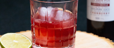 Verre déposé sur une planche de bois, rempli d'un amaretto sans alcool et une bouteille de jus canneberge 100% pur par CANNE BERGE