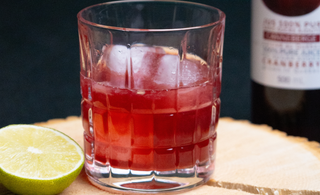 Verre déposé sur une planche de bois, rempli d'un amaretto sans alcool et une bouteille de jus canneberge 100% pur par CANNE BERGE