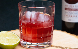 Verre déposé sur une planche de bois, rempli d'un amaretto sans alcool et une bouteille de jus canneberge 100% pur par CANNE BERGE