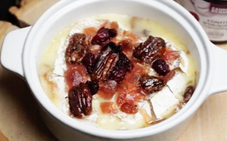 bol de brie fondant recouvert de cannebergers séchées et de pacanes à l'érable sur une planche de bois. Un pot de confit d'oignon CANNE BERGE à côté du bol.