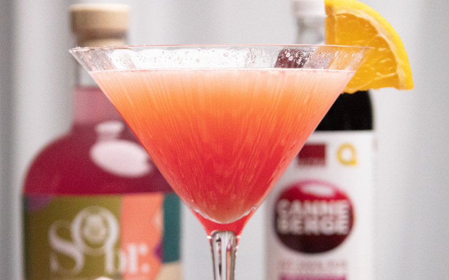 Verre de martini rempli de cosmopolitan sans alcool. Une bouteille de gin fruité sobr et une autre bouteille de jus pure de canneberge par CANNE BERGE. 