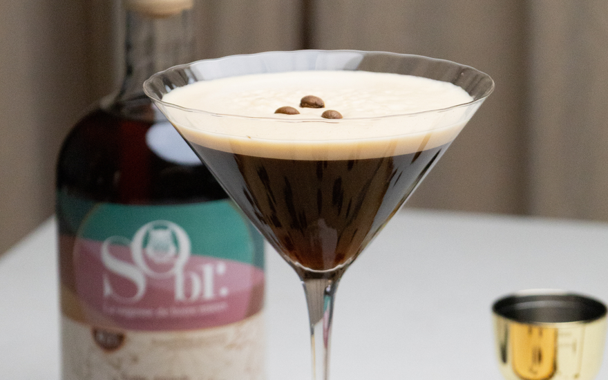 Verre de martini rempli d'un espresso martini sans alcool. Une bouteille d'amaretto érable et amande sans alcool par SObr.