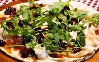 Pizza brie, roquette et canneberge déposée sur une planche de bois