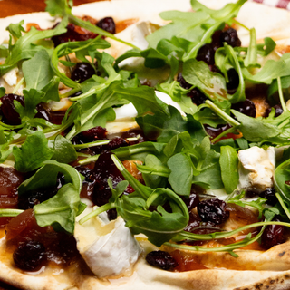 Pizza brie, roquette et canneberge déposée sur une planche de bois