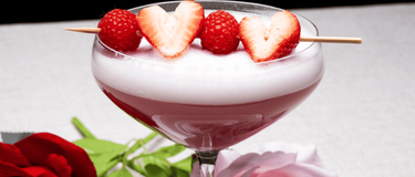 verre rempli du mocktail velours litchi et framboise avec une brochette de fraises et framboise