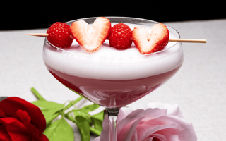 verre rempli du mocktail velours litchi et framboise avec une brochette de fraises et framboise